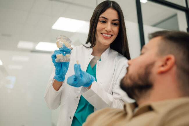 Dentist showing dental implant to patient in clinic The Dental Bridges